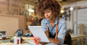 A woman in an apron focused on her tablet while working.